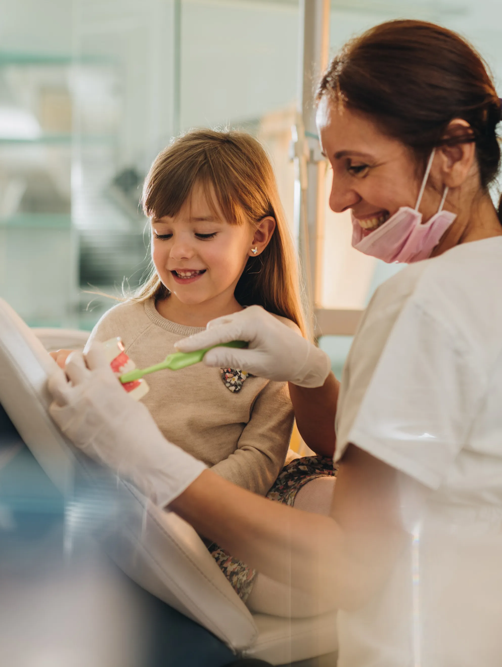 Smiling female dentist showing a young girl how to brush teeth using a dental model.