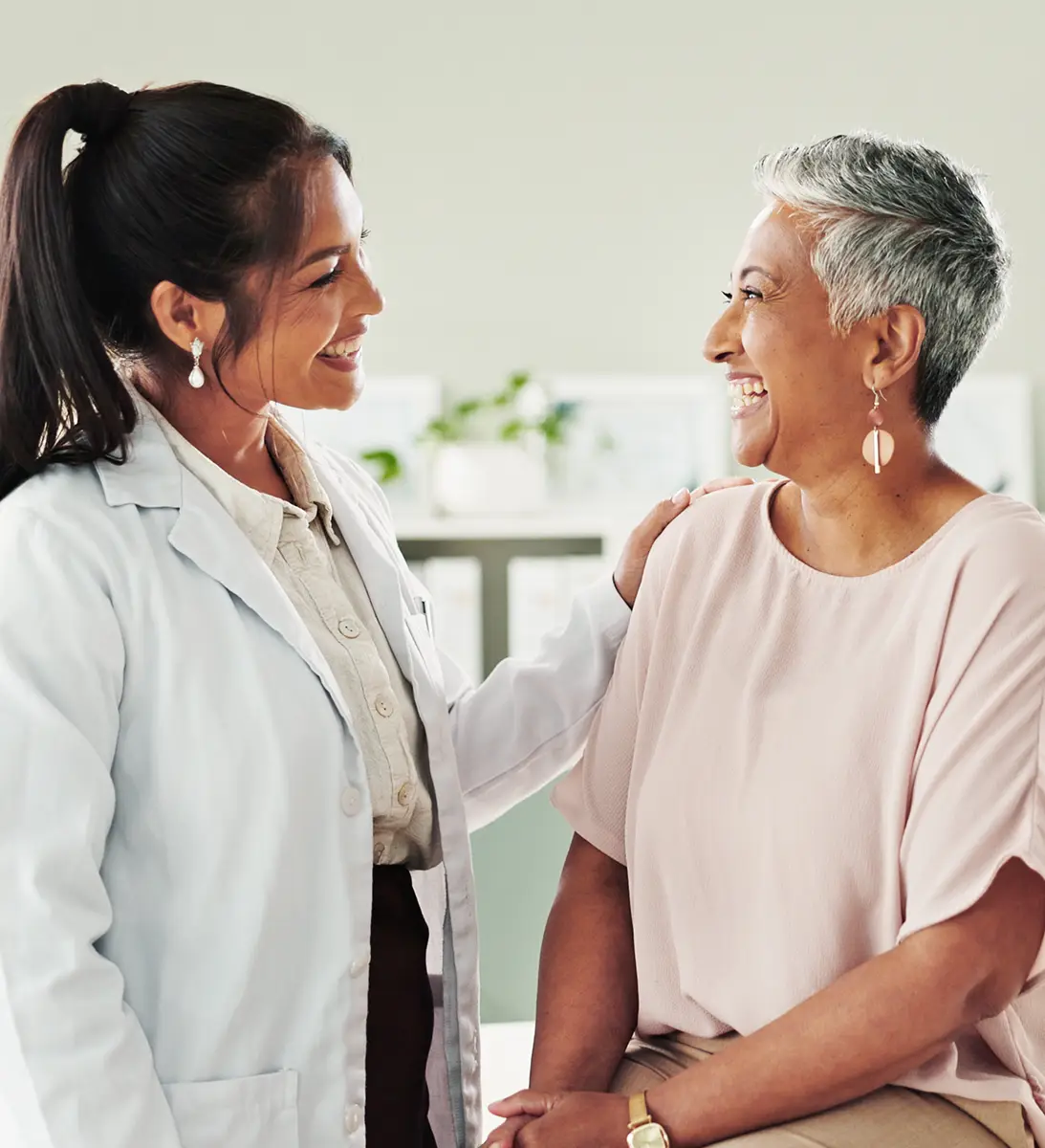 Female doctor smiling and placing hand on the shoulder of a seated senior woman in a light room.