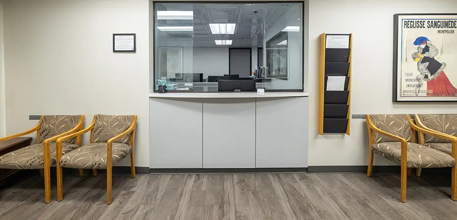Waiting area with patterned chairs, a reception window, brochure holder, and framed poster on the wall.