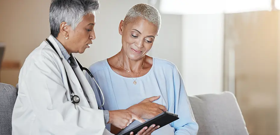 Doctor explaining medical information on a tablet to a smiling patient on a couch.