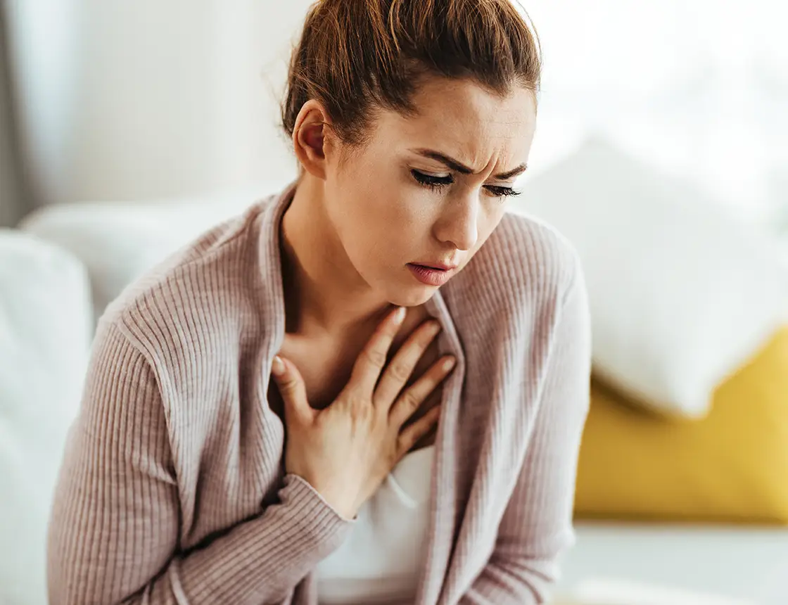 Woman holding her chest with a pained expression, suggesting discomfort or heart pain.