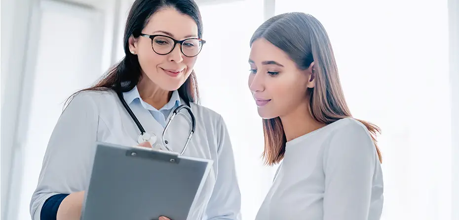 Doctor with a stethoscope showing a clipboard to a patient in a bright medical office.