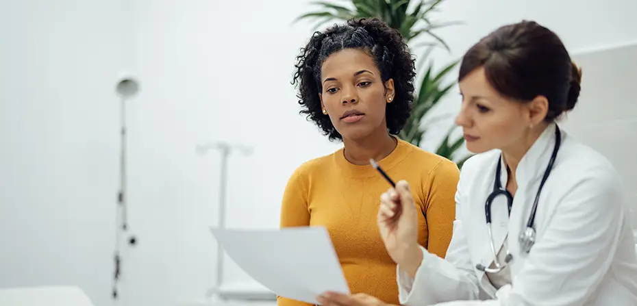 Doctor consulting attentive female patient, discussing document in a medical office.