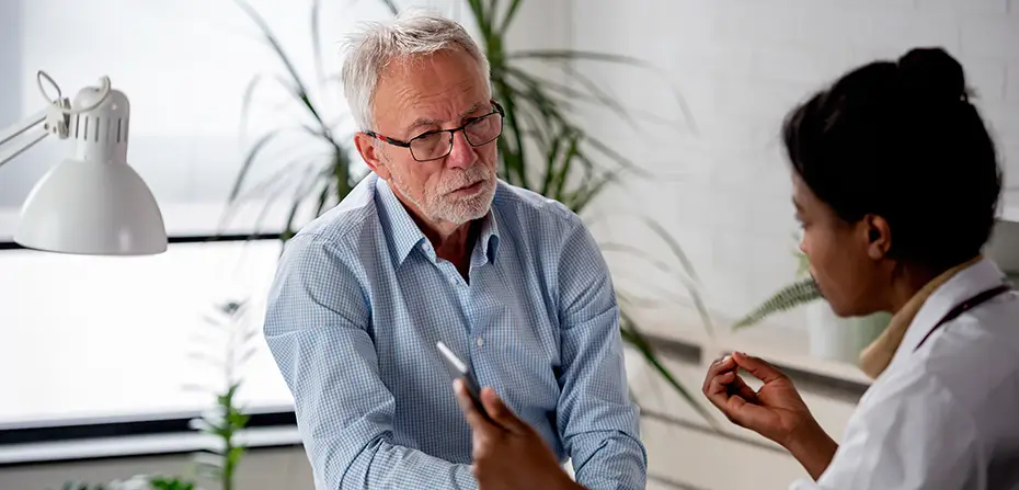 Senior man with glasses consulting a female doctor in a bright office setting.