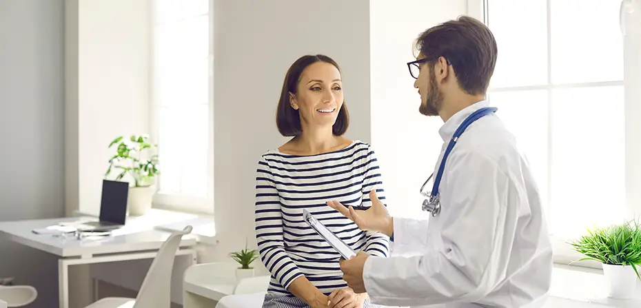 Female patient smiling while consulting with a male doctor in a bright medical office.