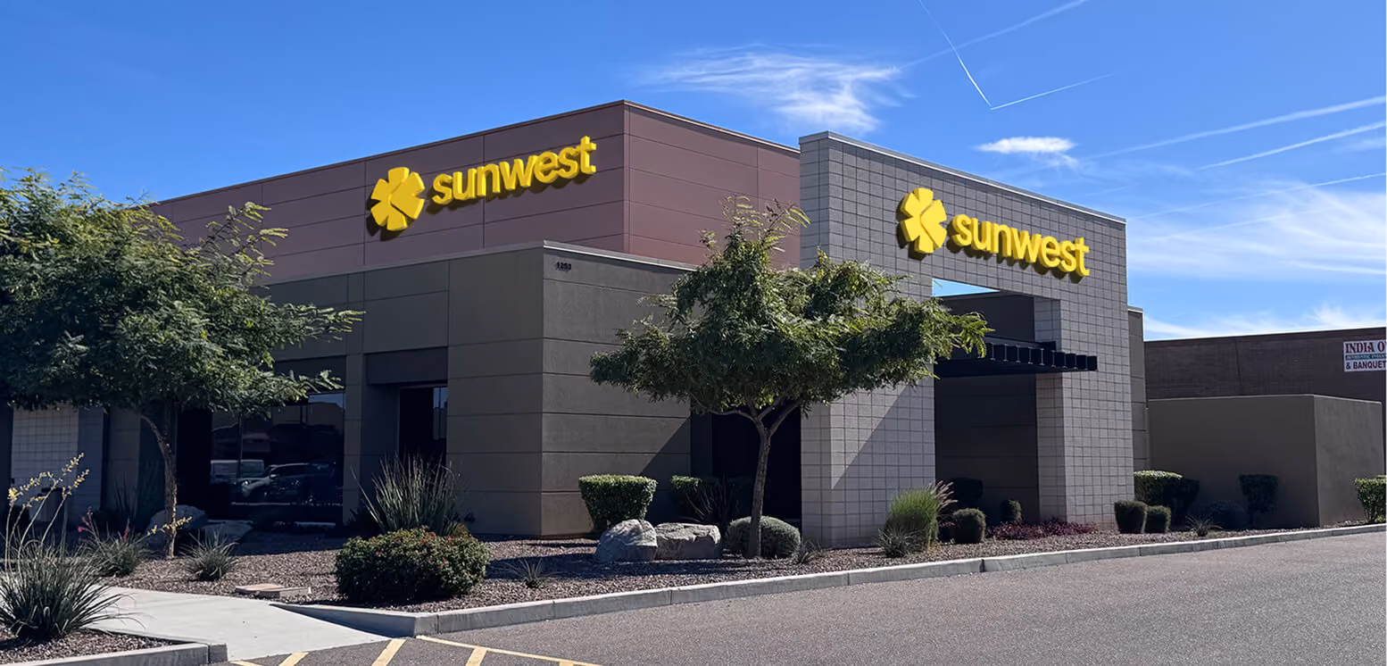 Modern building with Sunwest signage and trees around under a blue sky.