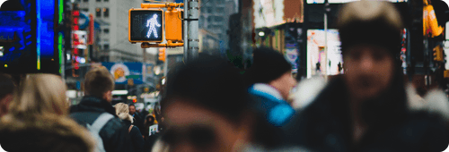 Crowd of people waiting at a pedestrian crossing with a walk signal showing white walking figure.