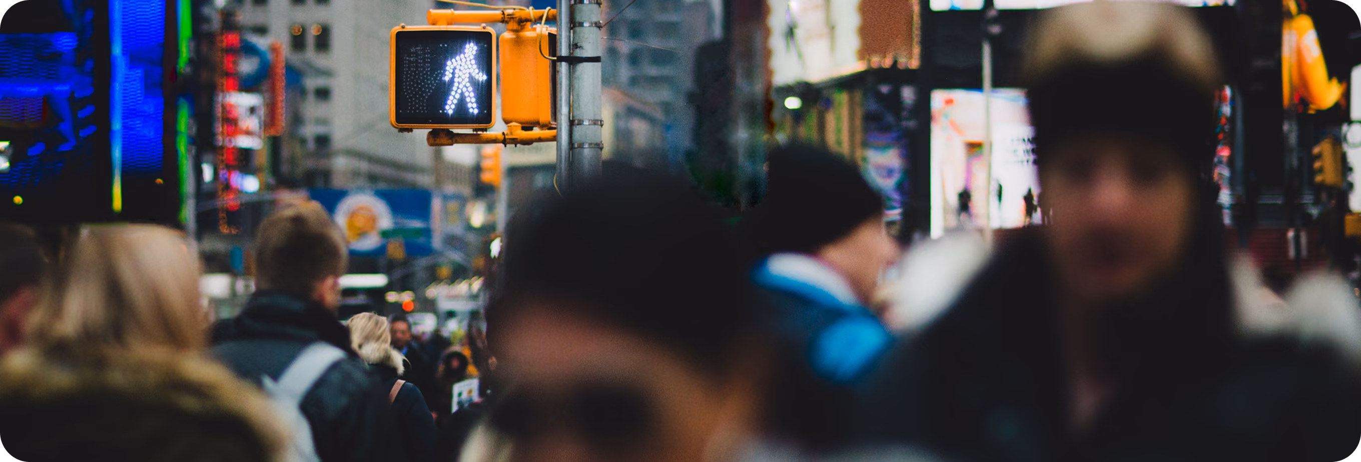 Crowd of people waiting at a pedestrian crossing with a walk signal showing white walking figure.