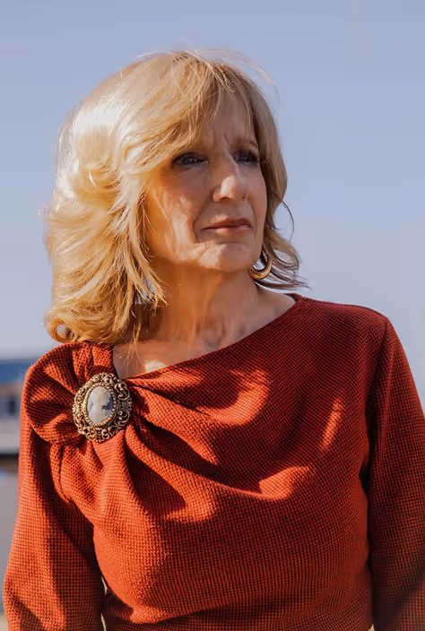 Blonde woman in red top with decorative brooch, looking to the side outdoors on a clear day.
