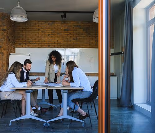 Team of five diverse colleagues in an office meeting room discussing documents around a table.