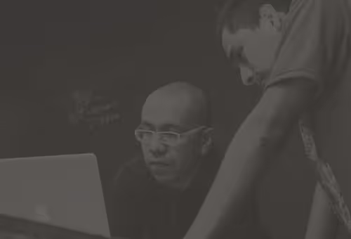 Two men focused on a laptop screen in a dimly lit room.