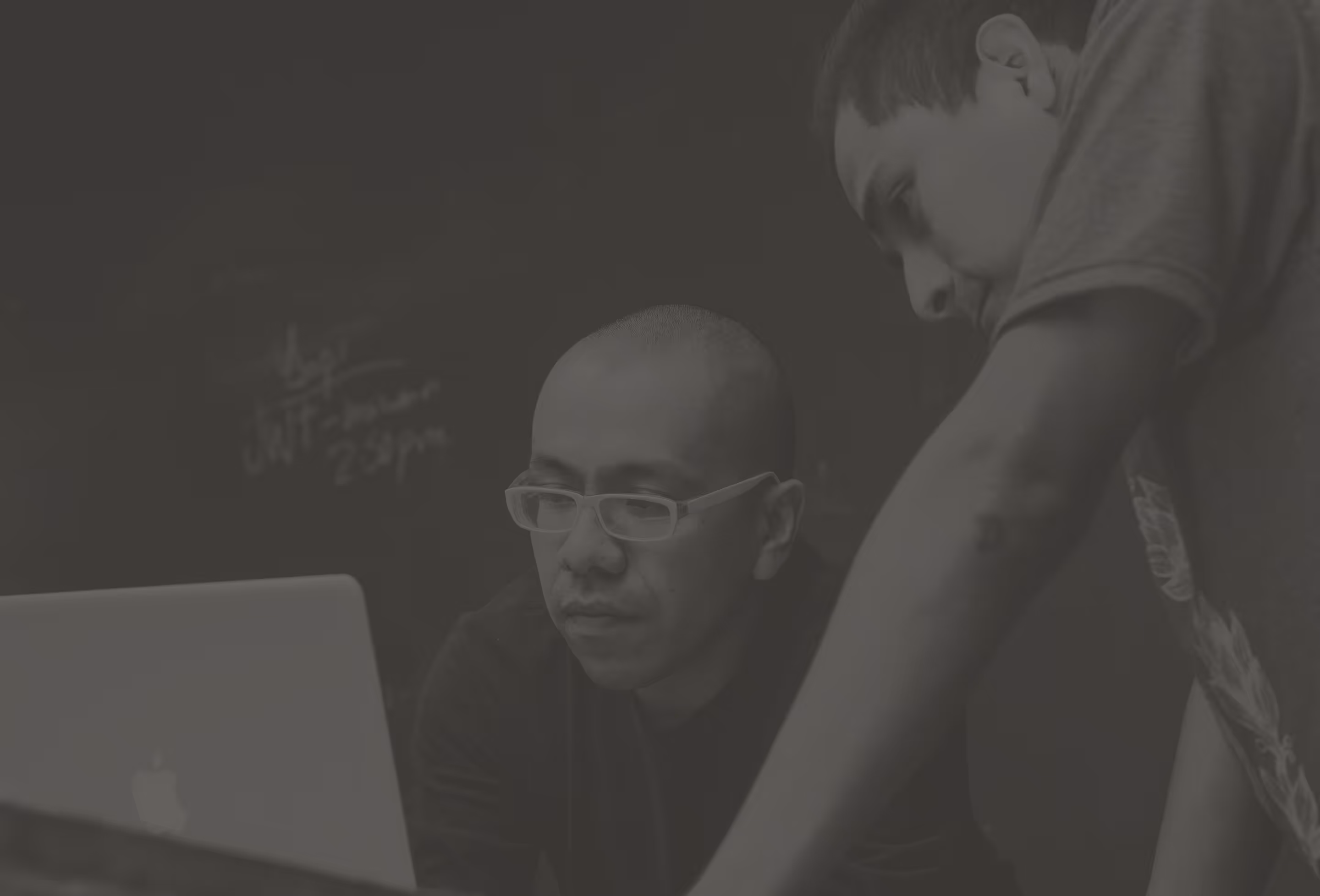 Two men focused on a laptop screen in a dimly lit room.