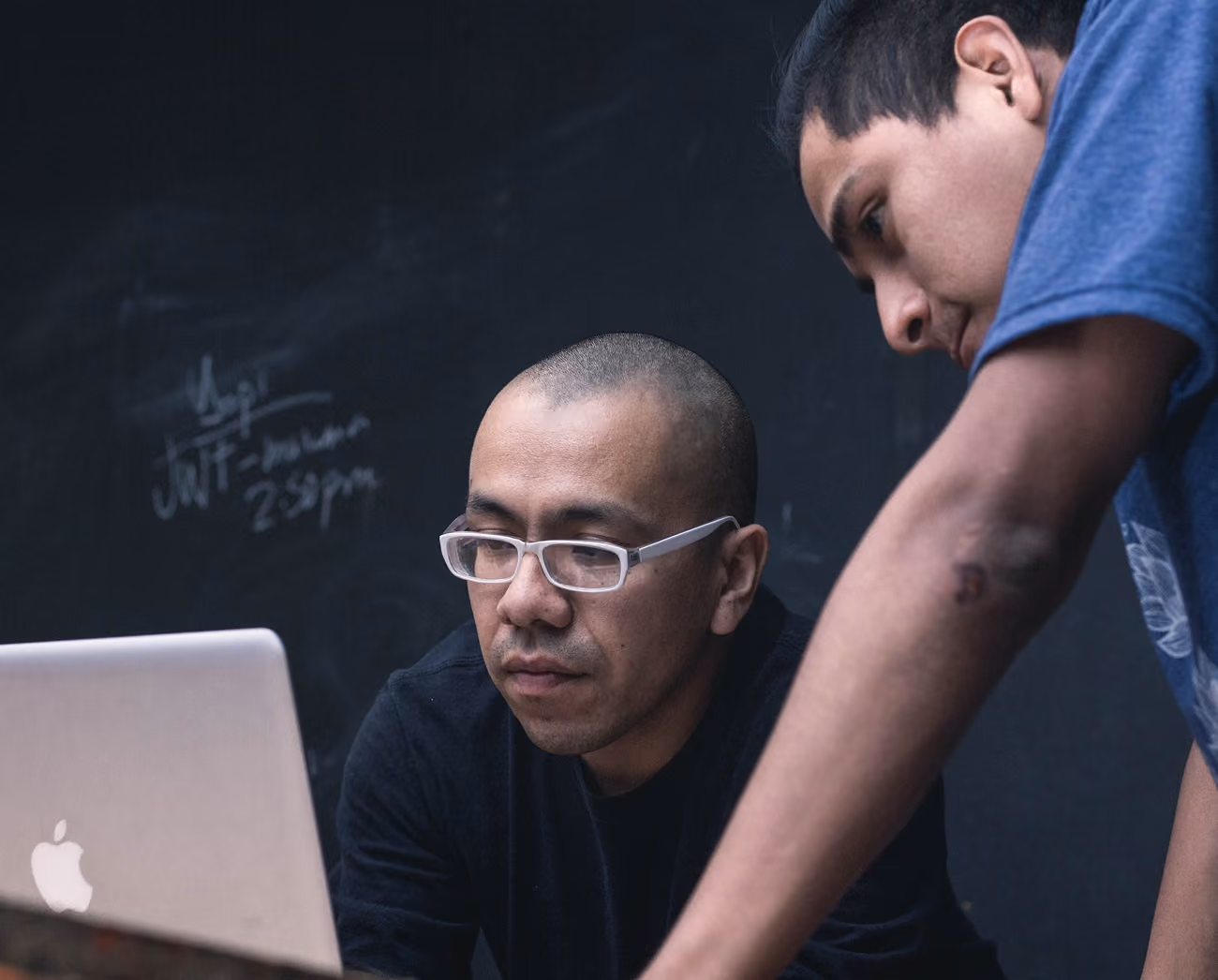 Two men focused on a laptop screen, one wearing glasses and the other leaning in closely.