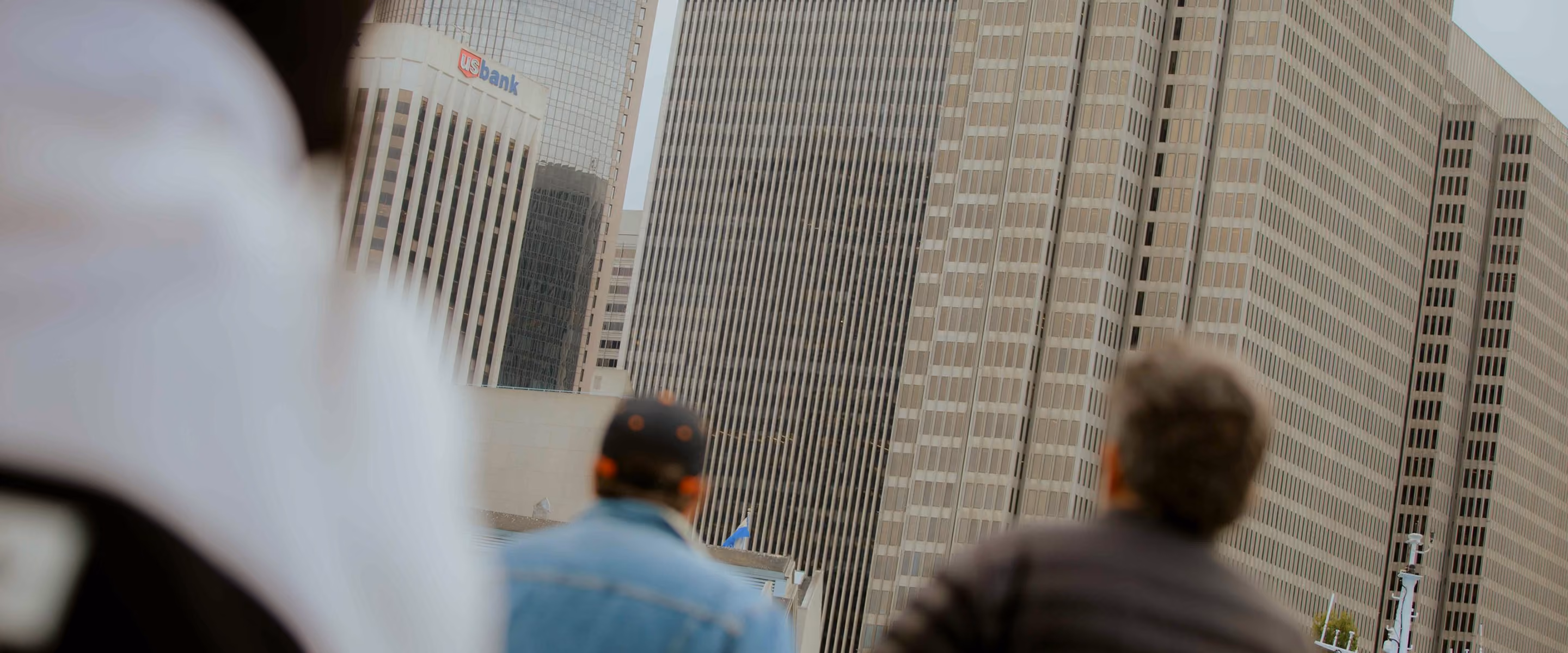 Two people seen from behind looking up at tall office buildings including one with a US Bank logo.