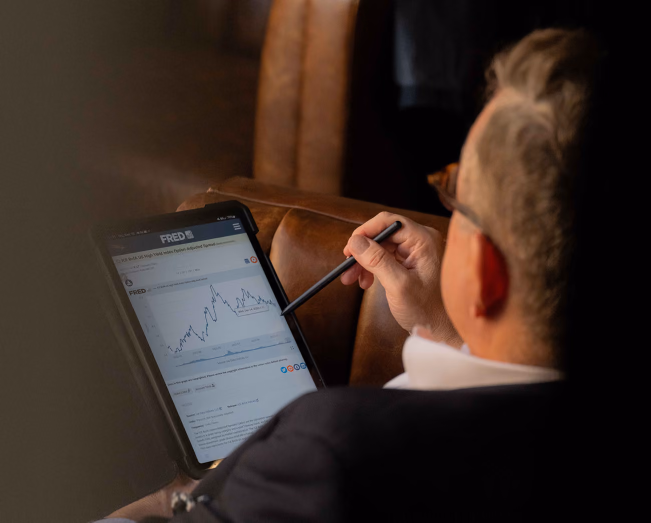Person holding a stylus pointing at a financial graph displayed on a tablet screen.