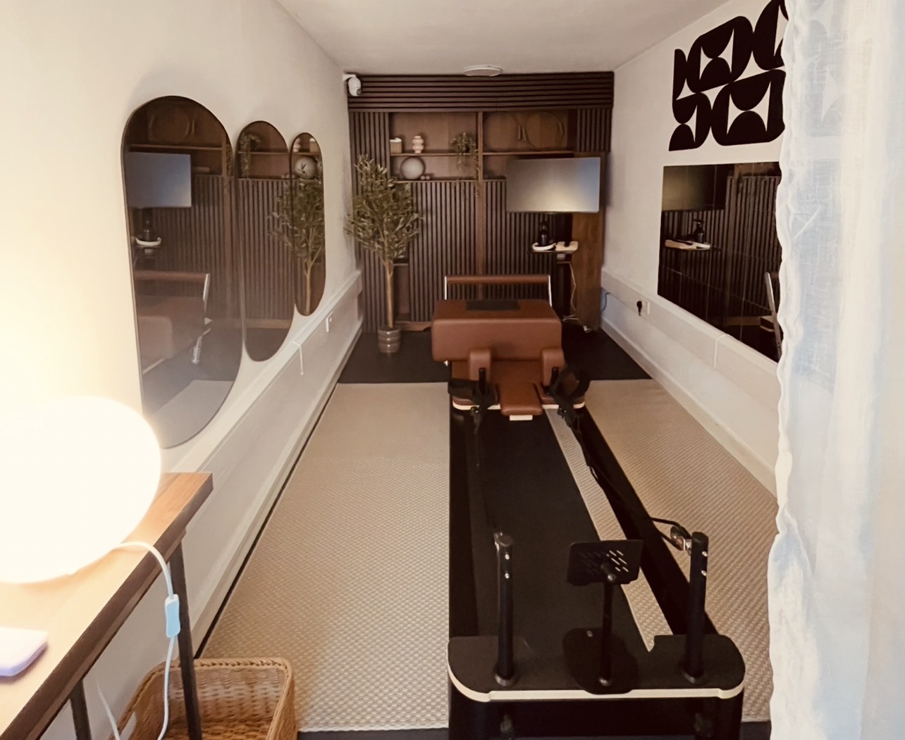 Modern Solo Movement private reformer studio with brown equipment, mirrors, plants, and wooden shelving.