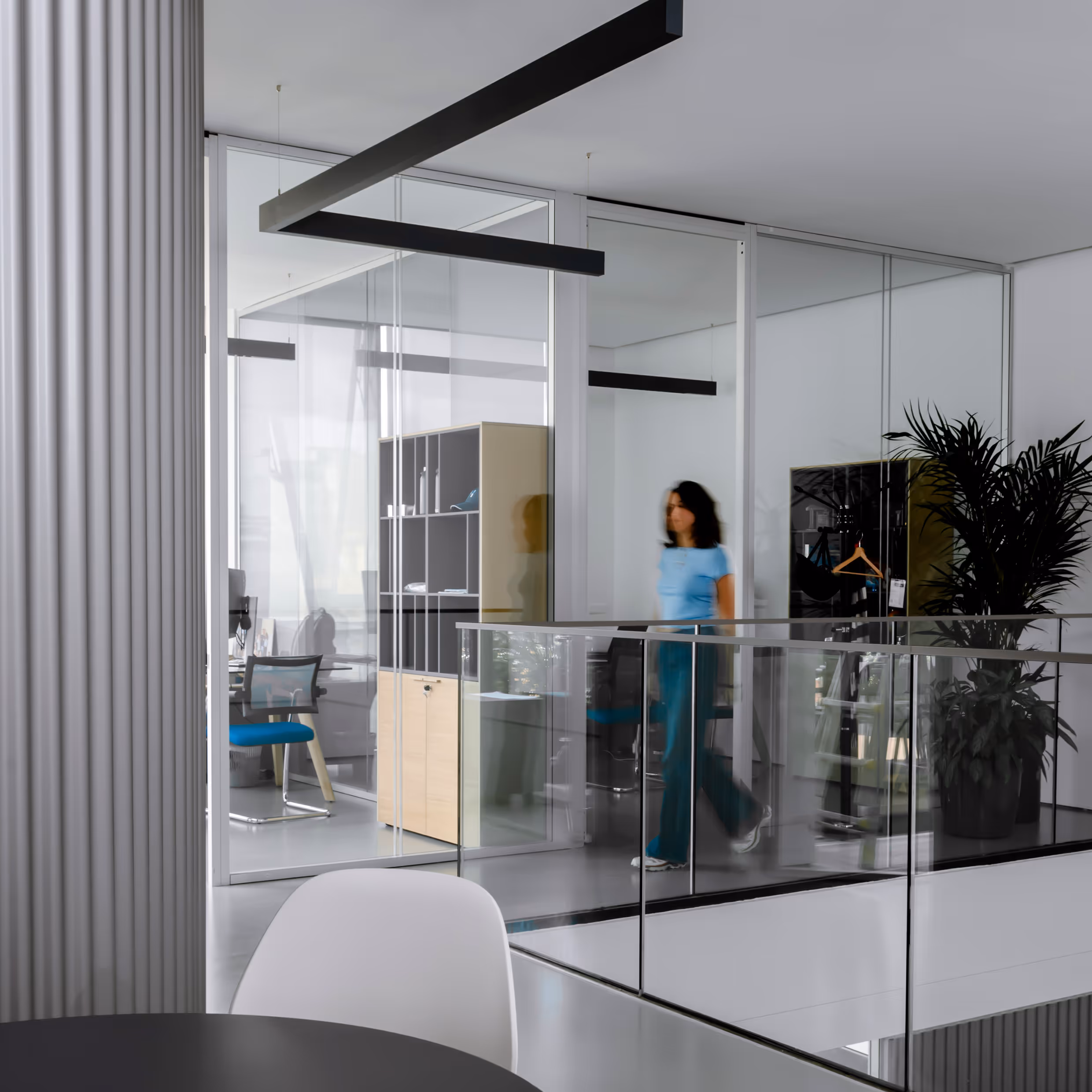 Modern glass-walled office interior with a person walking through a minimalist workspace