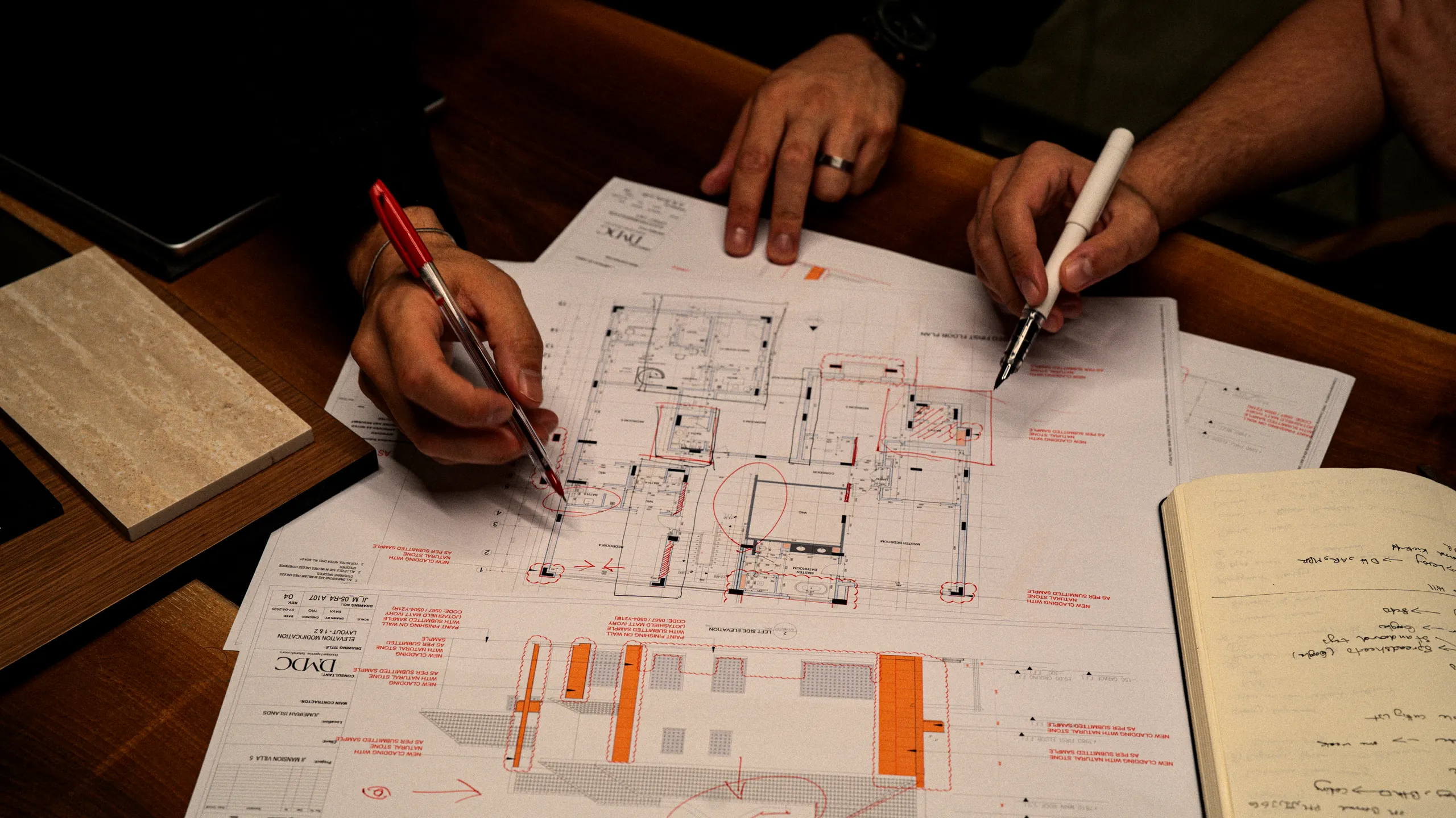 A hand drawing on a villa floor plan in raking morning light, with stone and timber samples and a steel scale rule on the desk