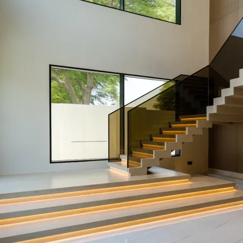 A stone staircase with lit treads and a glass balustrade in a double-height hall