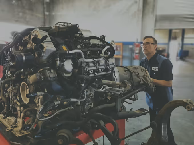 Mechanic examining a large engine mounted on a red engine stand in a workshop.