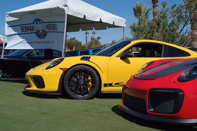 Yellow sports car and red sports car displayed on grass under a tent with a German Motors sign.