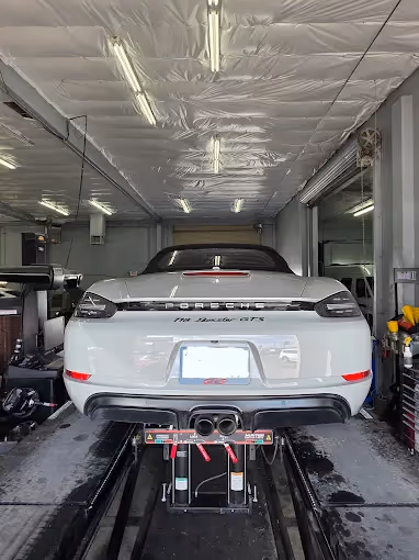 Rear view of a white Porsche 718 Boxster GTS on a car lift inside a garage.