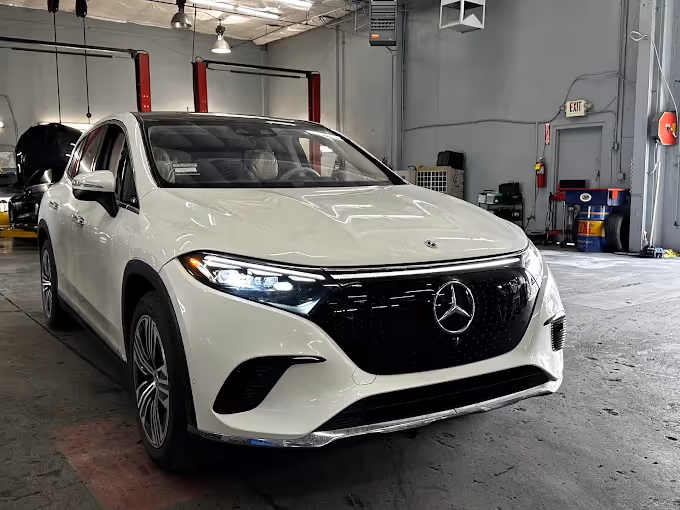 White Mercedes-Benz electric SUV inside a garage with lights on and visible front grille emblem.