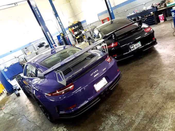 Black and purple Porsche GT3 RS cars parked inside a garage with workshop lifts and tools.