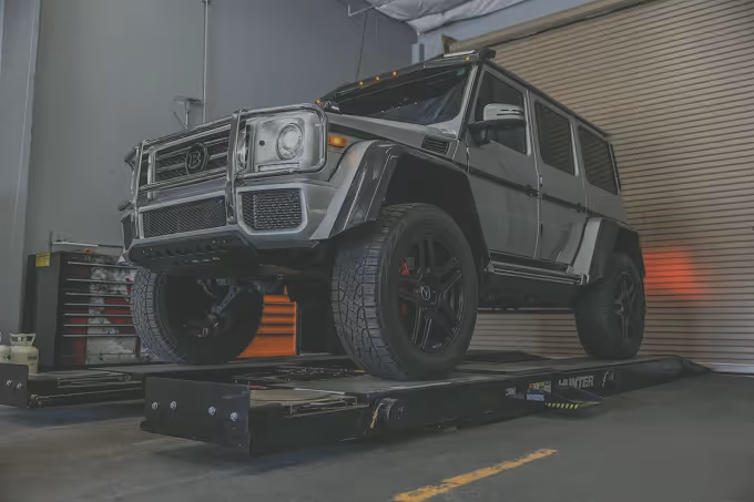 Silver Brabus G-Wagon SUV on a black vehicle lift inside a garage with a closed roller door.