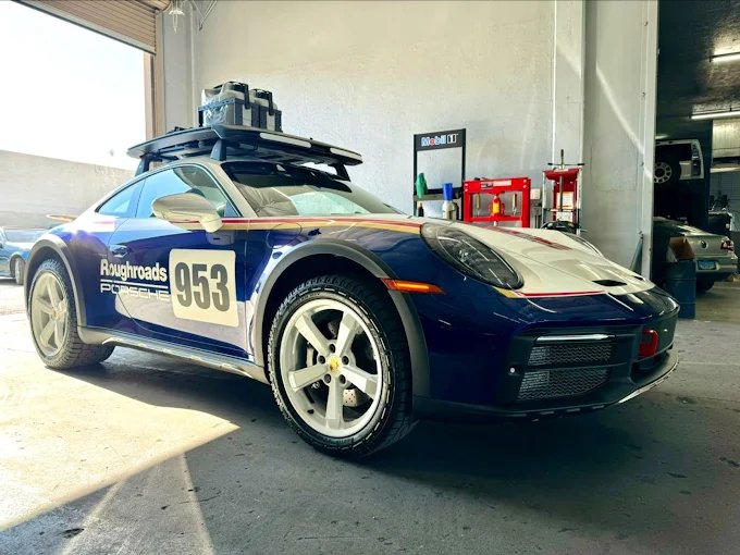 Blue and white Porsche sports car with number 953 and roof rack inside a garage.