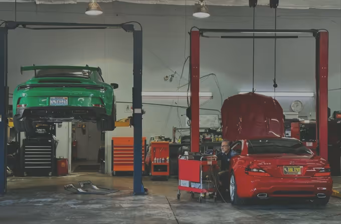 Green car elevated on lift and red car with open hood in a spacious auto repair garage.