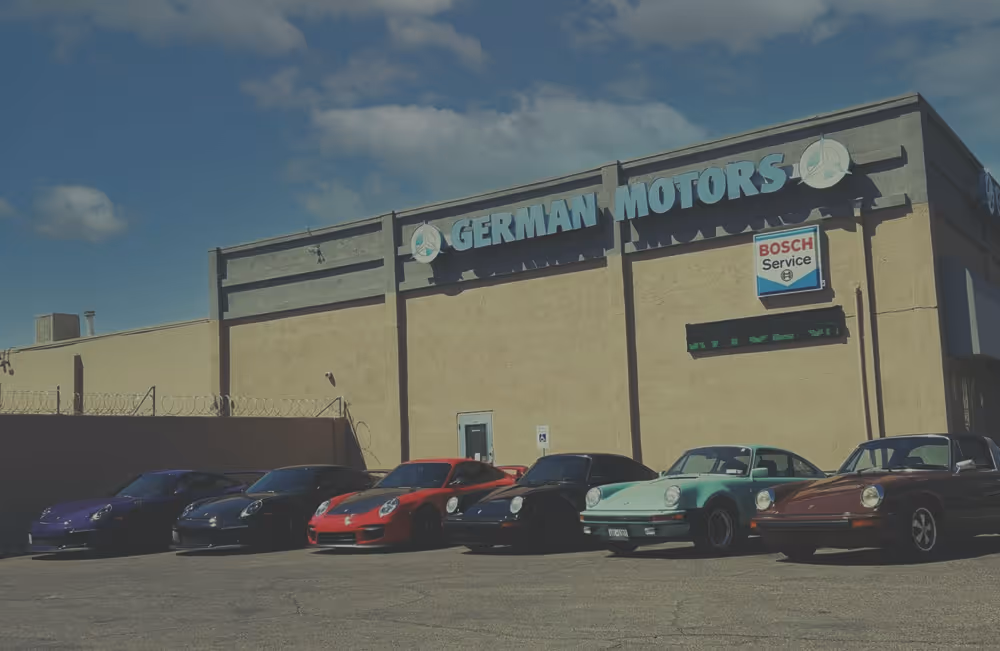 Six Porsche cars parked side by side outside a building labeled German Motors with Bosch Service sign.