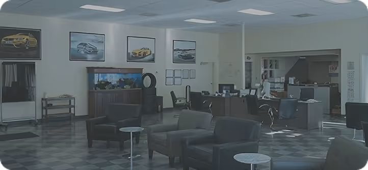 Car dealership waiting area with leather chairs, tables, framed car pictures, and a fish tank.