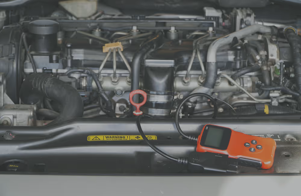 Car engine compartment with a red electronic diagnostic tool placed on front frame near a red dipstick.