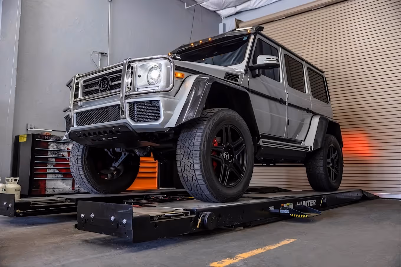Silver SUV on a vehicle alignment lift inside a garage with a rolled-down shutter door.