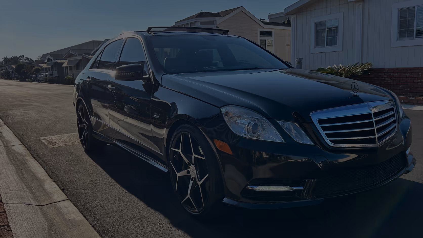 Black Mercedes-Benz sedan parked on a residential street near houses in daylight.