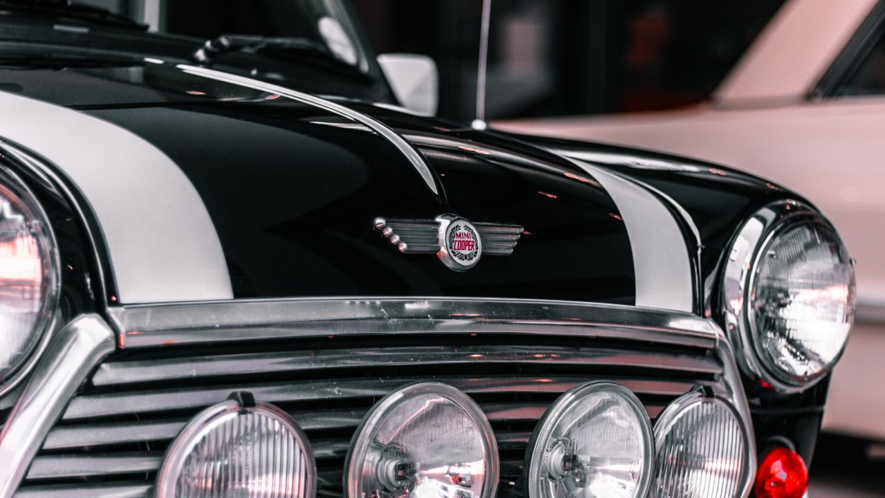 Front view of a black Mini Cooper car with white racing stripes and multiple round headlights.