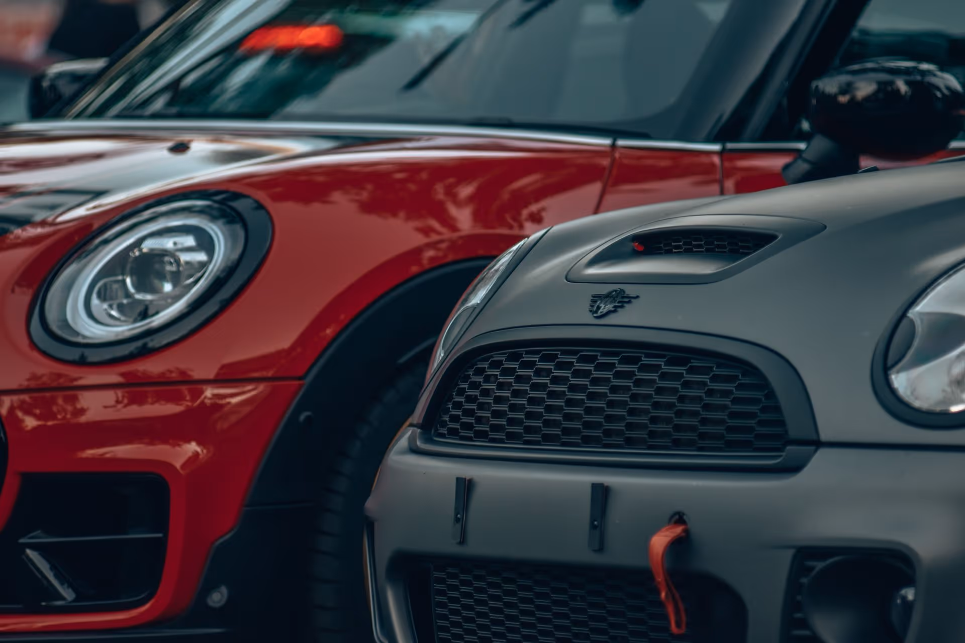 Close-up of the front ends of a red and a matte gray Mini Cooper car parked side by side.