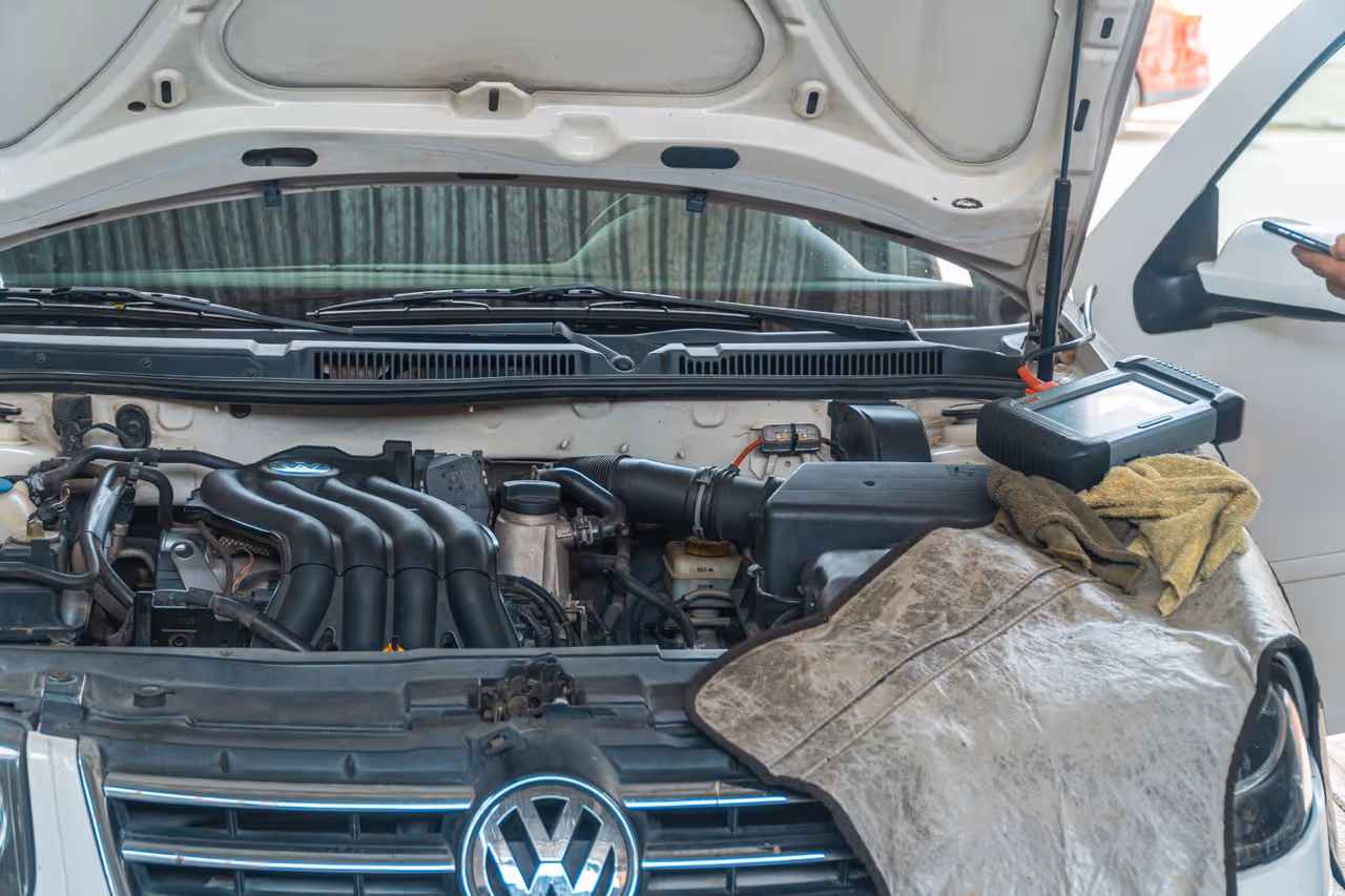 Open hood of a Volkswagen car showing engine with diagnostic tool and cloth on the front.