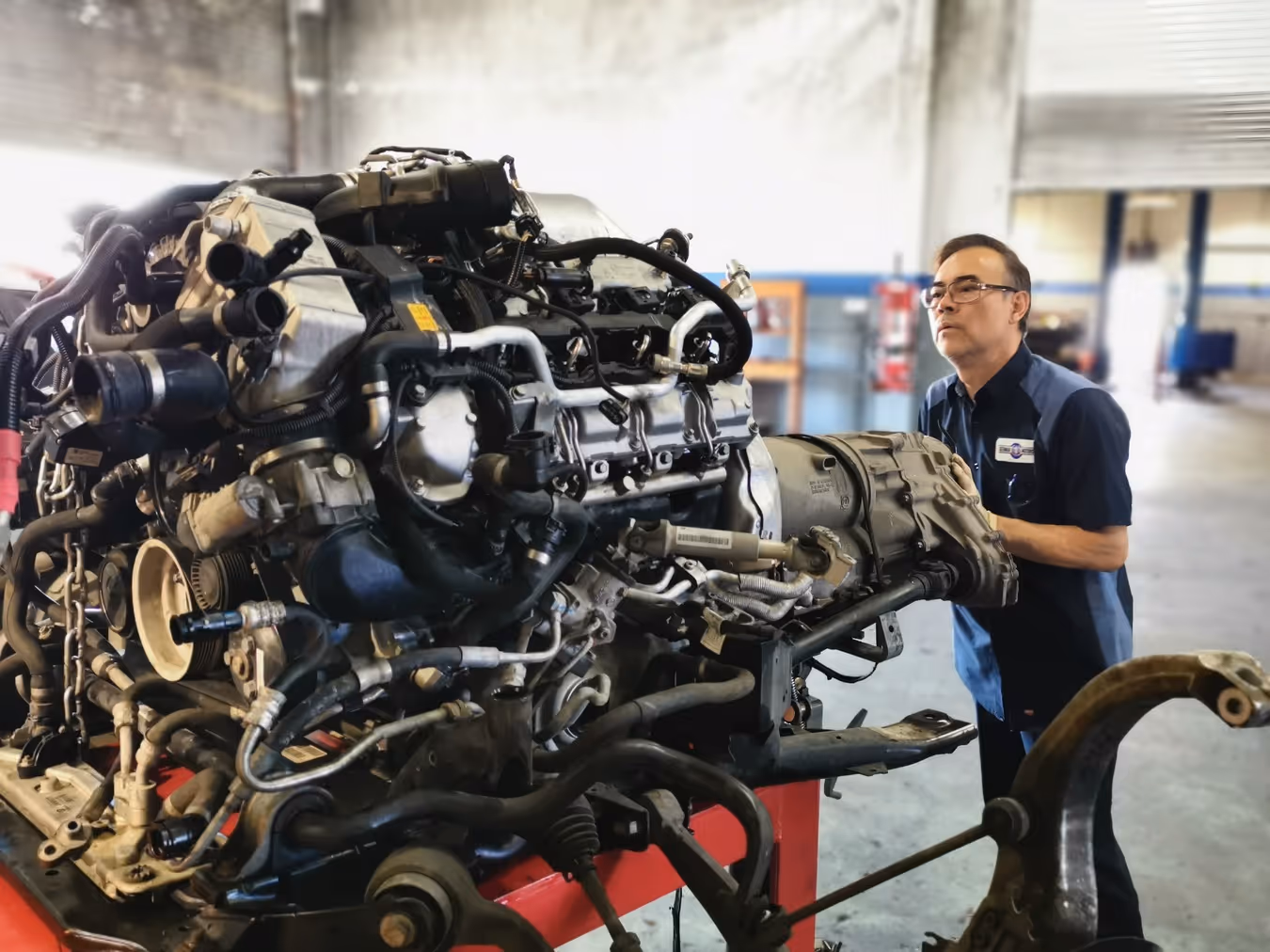 Mechanic wearing glasses inspecting a large car engine in a spacious auto repair shop.