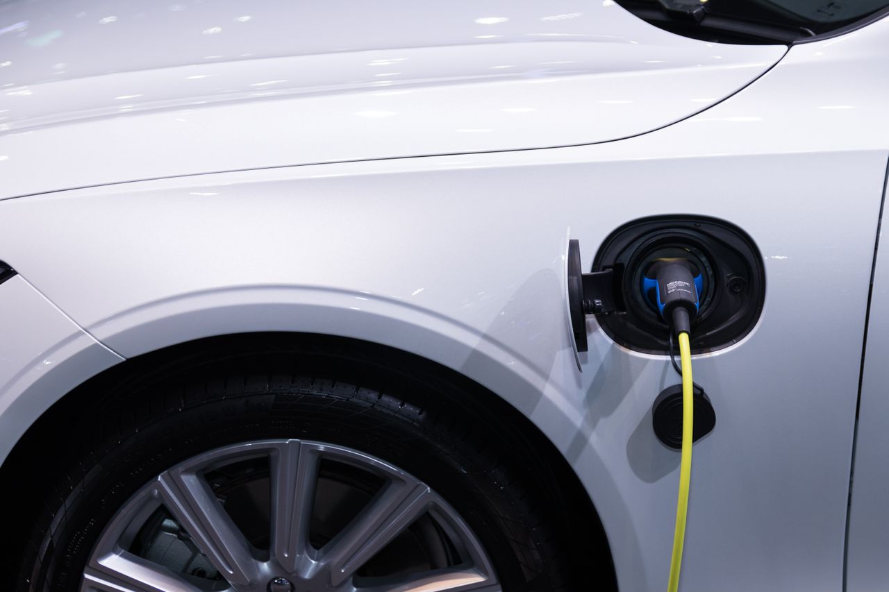 White electric car charging with a yellow cable connected to its side port near the front wheel.