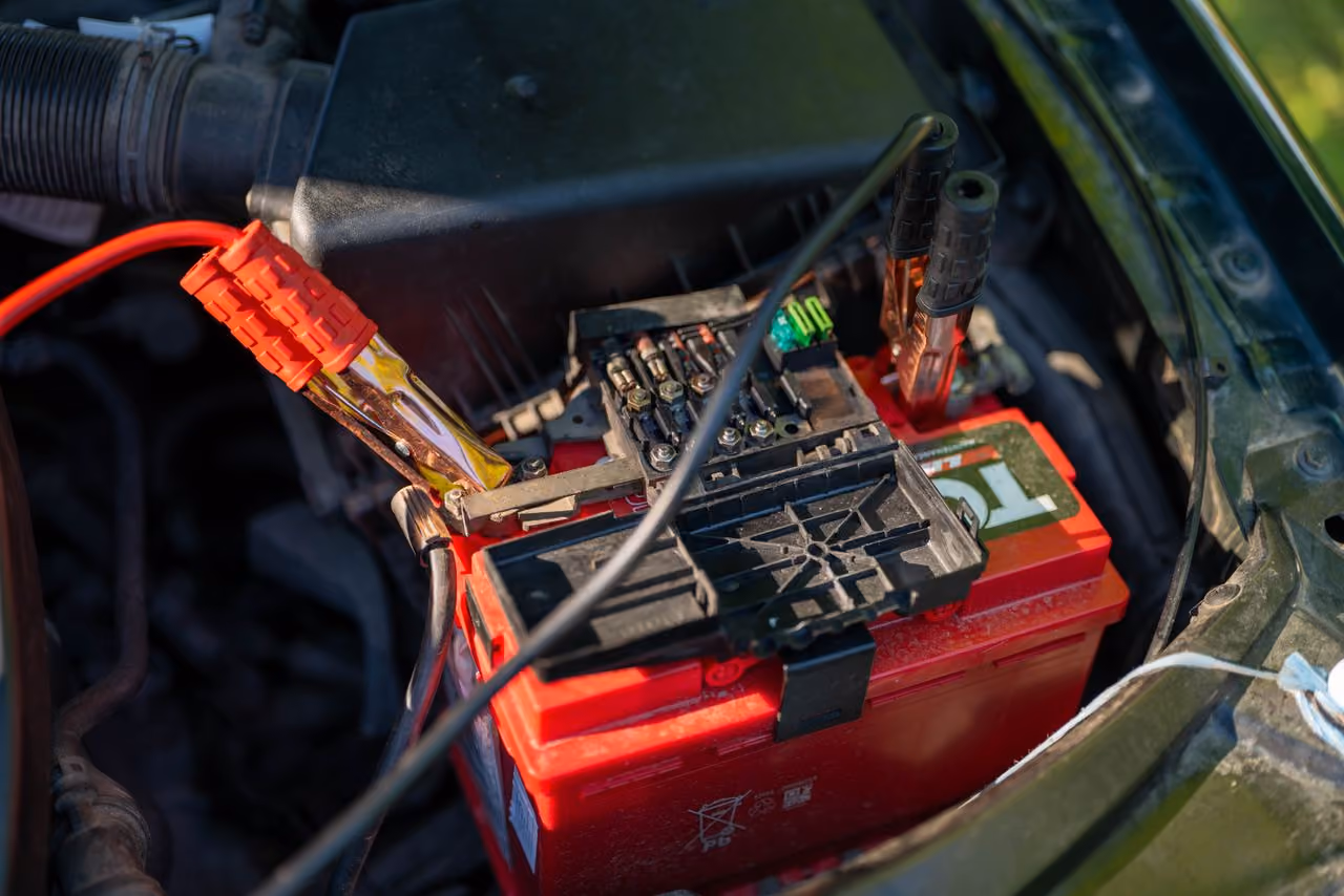 Car battery connected to jumper cables with red and black clamps attached to terminals.