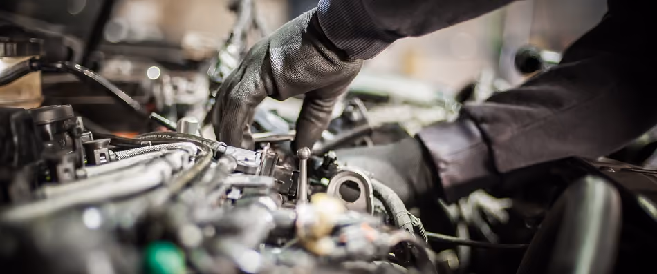 Mechanic wearing gloves working on a car engine during an oil change service.