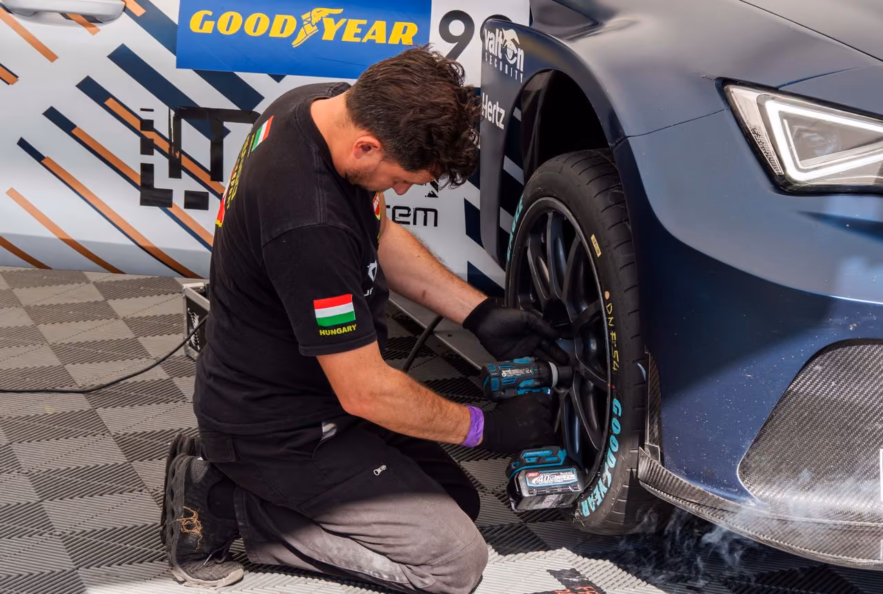 Man with gloves kneels using power tool to tighten lug nuts on race car's Goodyear tire.