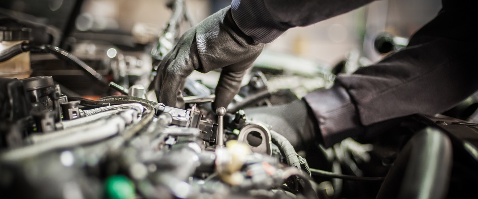Person wearing gloves fixing a car engine with tools under the hood.