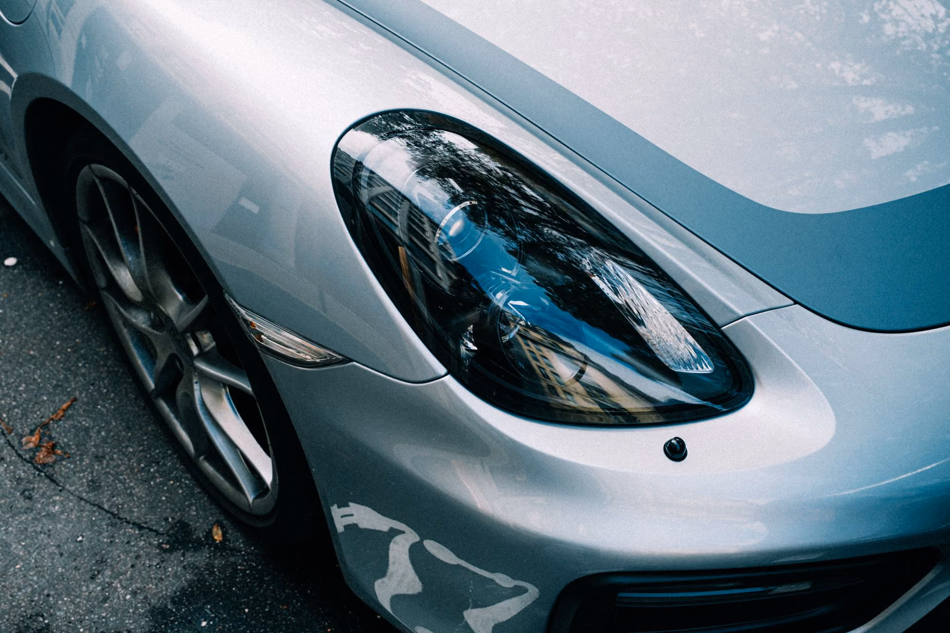 Close-up of a silver car's front headlight, wheel, and part of the hood with reflections.