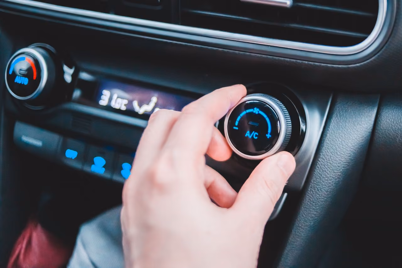 Hand adjusting car air conditioning dial with digital display showing 31 degrees Celsius.