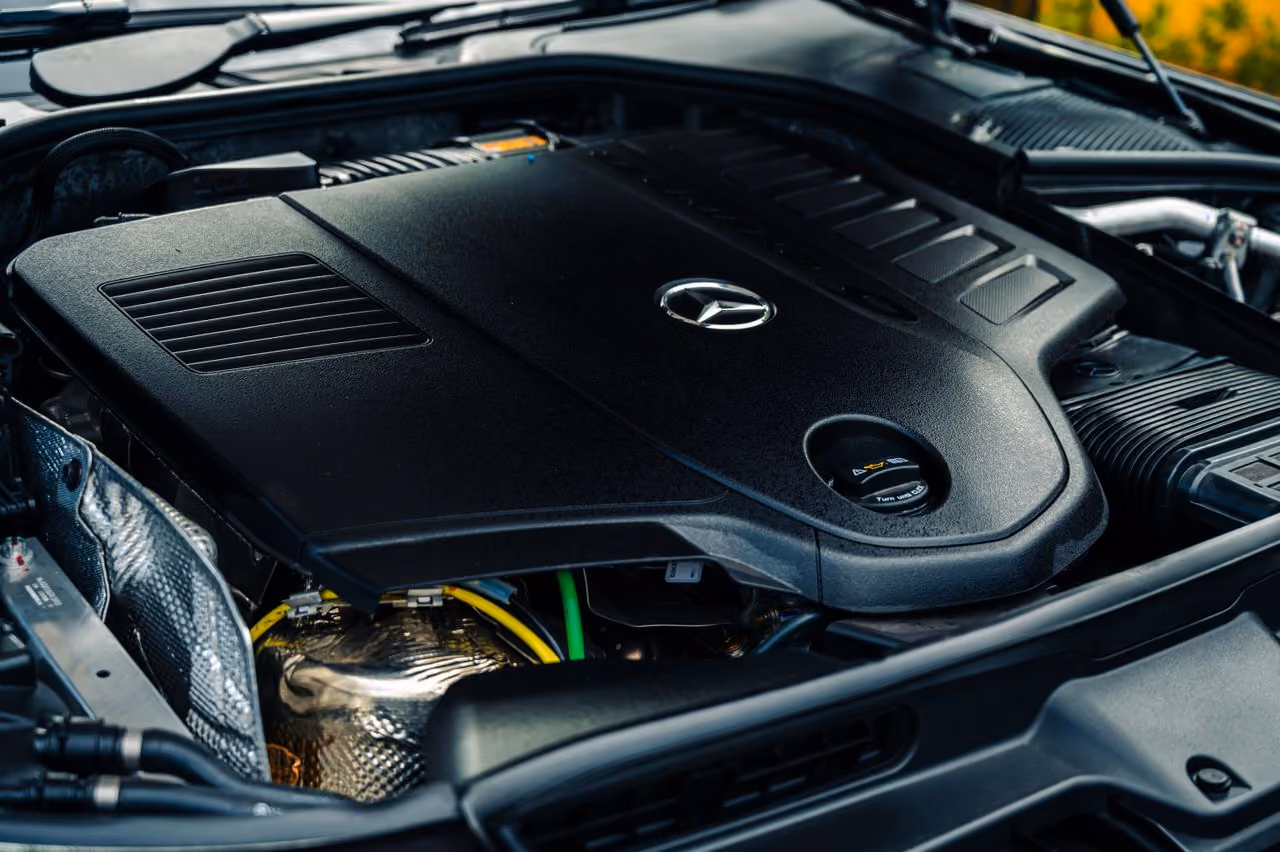 Close-up of a Mercedes-Benz car engine covered by a black plastic engine cover with the logo visible.