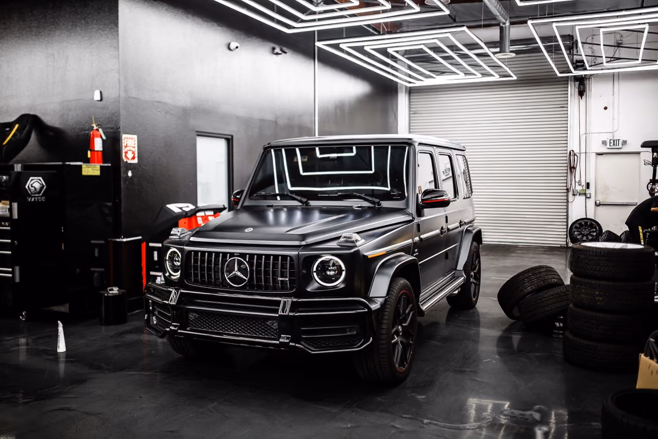 Black Mercedes G-Class SUV inside a modern garage with stacked tires and industrial lighting.