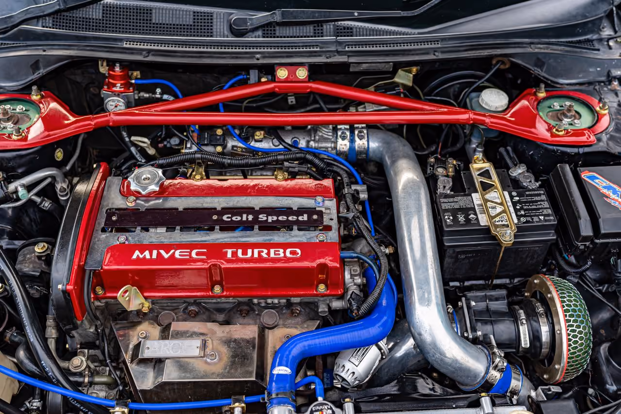 Close-up of a red MIVEC TURBO Colt Speed engine with blue hoses and metal parts inside a car.